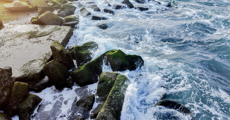 Mossy ocean boulders with dynamic waves crashing against them at sunset, ideal for backgrounds and nature-themed designs with space for text on the right