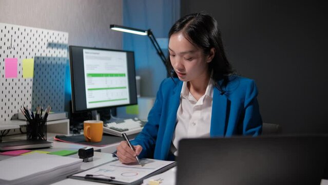 A young female employee is sitting in her private office working on various documents assigned by her boss that must be completed on time, lot of documents on the table while business woman worked.