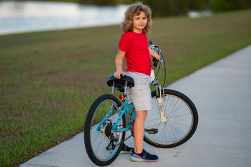 Sporty kid riding bike on a park. Child riding bicycle. Kid learns to ride a bike. Kids on bicycle. Happy child in t-shirt cycling outdoor. Sports leisure with kids.