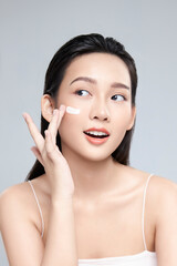 Beauty portrait image of pretty asian woman smiling and applying face cream isolated over light...