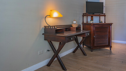 Details of the living room interior in retro style. There is mahogany furniture against the wall. There is a tea set on the chest, a TV. There is a lighted lamp on the table, a wicker basket.