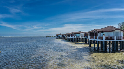 A row of water villas on stilts in the ocean. White houses with tiled roofs and terraces against...
