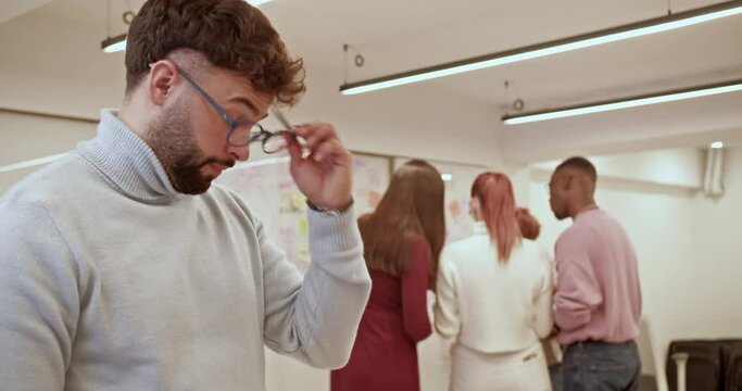 Young, male, business entrepreneur taking a deep breath, his eyeglasses off and rubbing his eyes during rough night shift at the office.