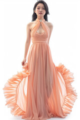 Portrait of a pretty young woman super model of Korean ethnicity draped in an ethereal peach chiffon gown with a halter neckline, gathered waist, and cascading ruffles