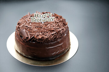 A dark black forest chocolate cake with a Happy Birthday sign sits on a black background