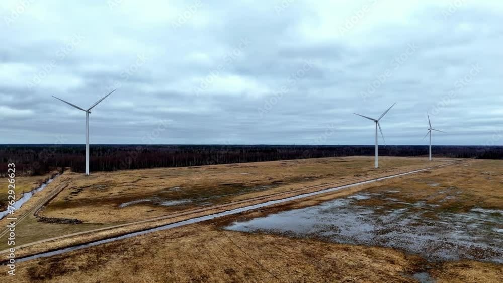 Poster aerial field with three wind turbines in the background. the sky is cloudy and the wind turbines are