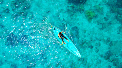 Aerial view of a woman kayaking in the blue sea and clear water. You can see corals under the sea.	