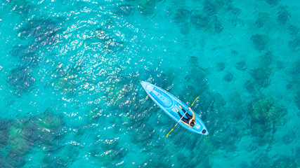Aerial view of a woman kayaking in the blue sea and clear water. You can see corals under the sea.