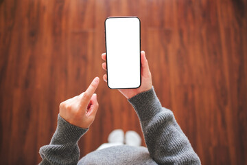 Top view mockup image of a woman holding and pointing at mobile phone with blank desktop white...