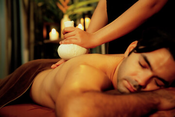 Hot herbal ball spa massage body treatment, masseur gently compresses herb bag on man body....