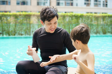 Father is applying a sun screen or sun block lotion on his son body before going to swimming in the...