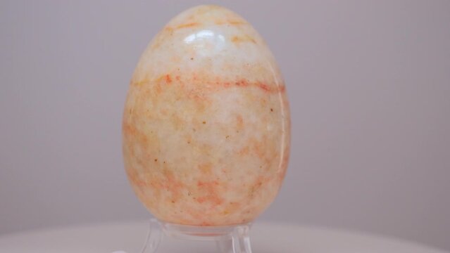 Orange and cream Marble egg rotating slowly on a turntable in front of a white background.