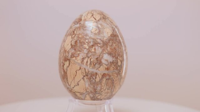 Large fragmented Granite egg rotating slowly on a turntable in front of a white background.
