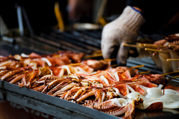  fresh squids is being grilled to a golden perfection on the barbecue grill - obrazy, fototapety, plakaty