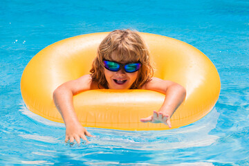 Child in sunglasses floating in pool. Little kid boy floating in a swimming pool on summer vacation. Happy kid playing with swim ring in swimming pool.