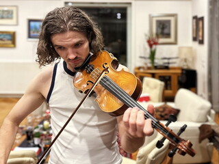 Young handsome man playing violin at home