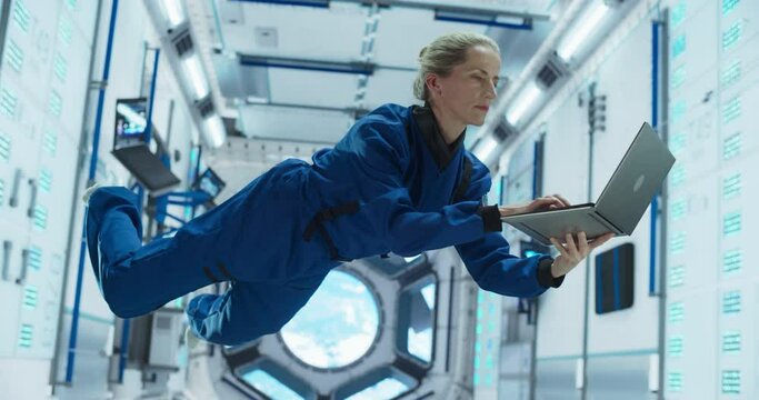 Female Astronaut Using a Laptop Computer in Space Inside a Spacecraft. Working Online, Checking and Updating Flight Information, Writing Report. Spacewoman Floating in Zero Gravity Inside a Spaceship 