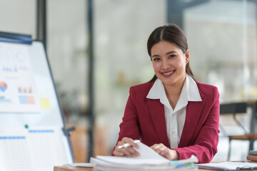Asian businesswoman in a red suit is smiling and writing on a piece of paper