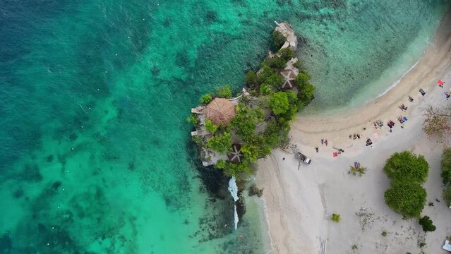 Top-down drone footage of a white beach with tourists and turquoise water on Siquijor in the Philippines, reverse way.