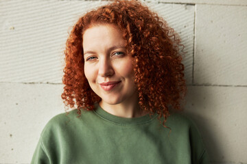 Charming coquettish woman with red curly hair winking at camera with sly cunning facial expression,...
