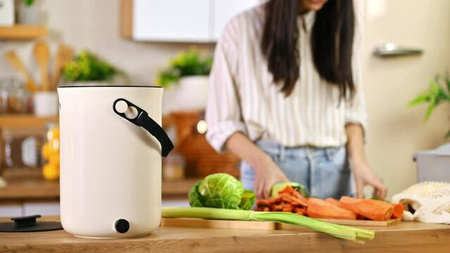 Young woman recycling vegetables peels in a compost bin. Housewife cooking food and composting organic waste in a bokashi container at home. Ecological and sustainability concept