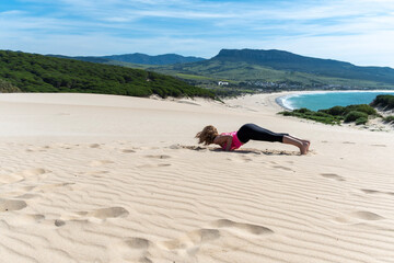  Mature Woman Practicing Yoga on  A mature woman performs a plank pose on the sandy Bolonia dune in...