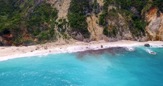 Drone panning in front of the rocky limestones behind the secluded Petanoi beachfront, located in the island of Kefalonia in the Western Coast of Greece.