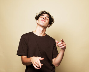 A smiling young man in a brown t-shirt dances on a beige studio background, enjoys life