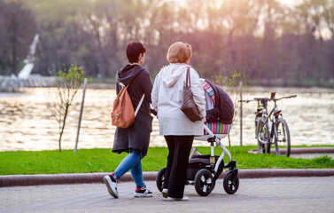 Two girls with a baby stroller are walking in the summer park
