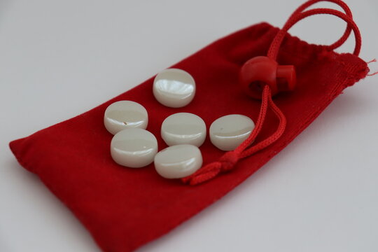 A game of mangala played with wood and marbles placed on a table, lined up on a red bag.