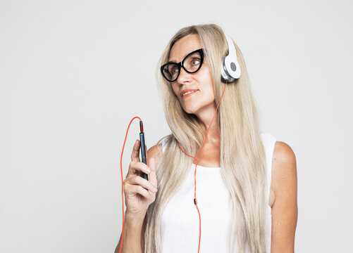 Senior woman wearing glasses listening to music with smartphone isolated on light grey background