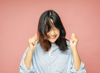 Young asian woman celebrates victory and success, feels lively and energetic over pink background