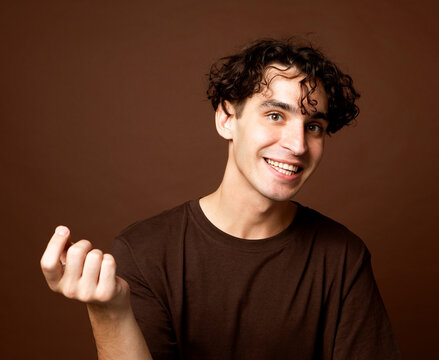 Handsome young smiling man wear brown t-shirt looking at camera on brown background