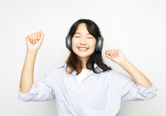 Pretty smiling Asian teenage girl listens to music on headphones over white background.