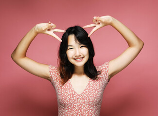 young asian woman wears pink dress showing victory sign