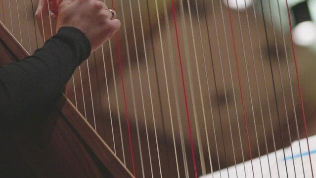 A slow motion video of a musician playing the harp by plucking the strings of the instrument during a classical symphony orchestra performance. Nr. 2
