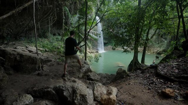 Man walking towards a beautiful waterfall during cloudy day.