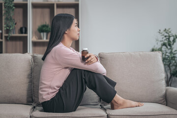 Obraz premium Young Asian woman sitting on sofa, depression, distressed, touches face and head, eyes closed. tired, sick, and stressed, possibly grappling with bad news or crisis, experiencing headache or migraine