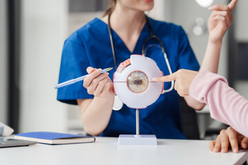 Female Caucasian ophthalmologist explains about eye diseases using the eye model with an Asian...
