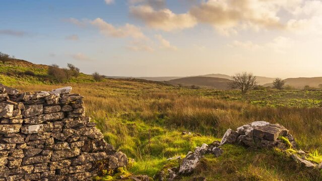Timelapse of rural nature farmland with old stonewall ruin in the foreground during dramatic cloudy sunset evening viewed from Carrowkeel in county Sligo in Ireland.