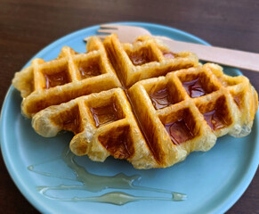 Closeup waffle topped with honey sauce on blue plate at cafe. Sweet bakery in dish on wooden table or background with copy space.