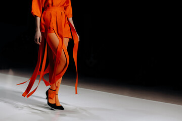 Trendy women's look orange tights and designer shorts, fashion model walking on the podium