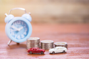 Toy car,alarm clock and coin stacks on wood table background.