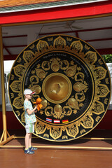Tourist kid, child and gong. Wat Phra Chetuphon Vimolmangklararm Rajwaramahaviharn (Wat Pho) Buddhist templein Bangkok city, Thailand. Religious traditional national Thai architecture. Landmark