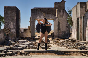Fototapeta na wymiar South American woman, young, beautiful, brunette with lingerie and black wings, posing in the middle of some ruined buildings in sensual and provocative attitude. Concept angels, beauty, costumes.