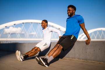 Two friends are exercising in the city. They are doing reverse push-ups.