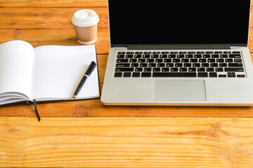 Laptop computer,pencil,cup of coffee and note pad on wood table