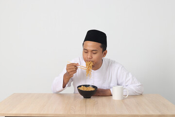 Fototapeta na wymiar Portrait of attractive Asian muslim man eating tasteful instant noodles with chopsticks served on bowl. Iftar and pre dawn meal concept. Isolated image on white background