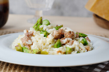 Italian Risotto with asparagus, sausage and parmesan cheese on white plate on table. 