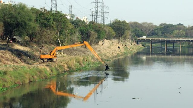Excavator dredging sediment mud from canal in Delhi, India.